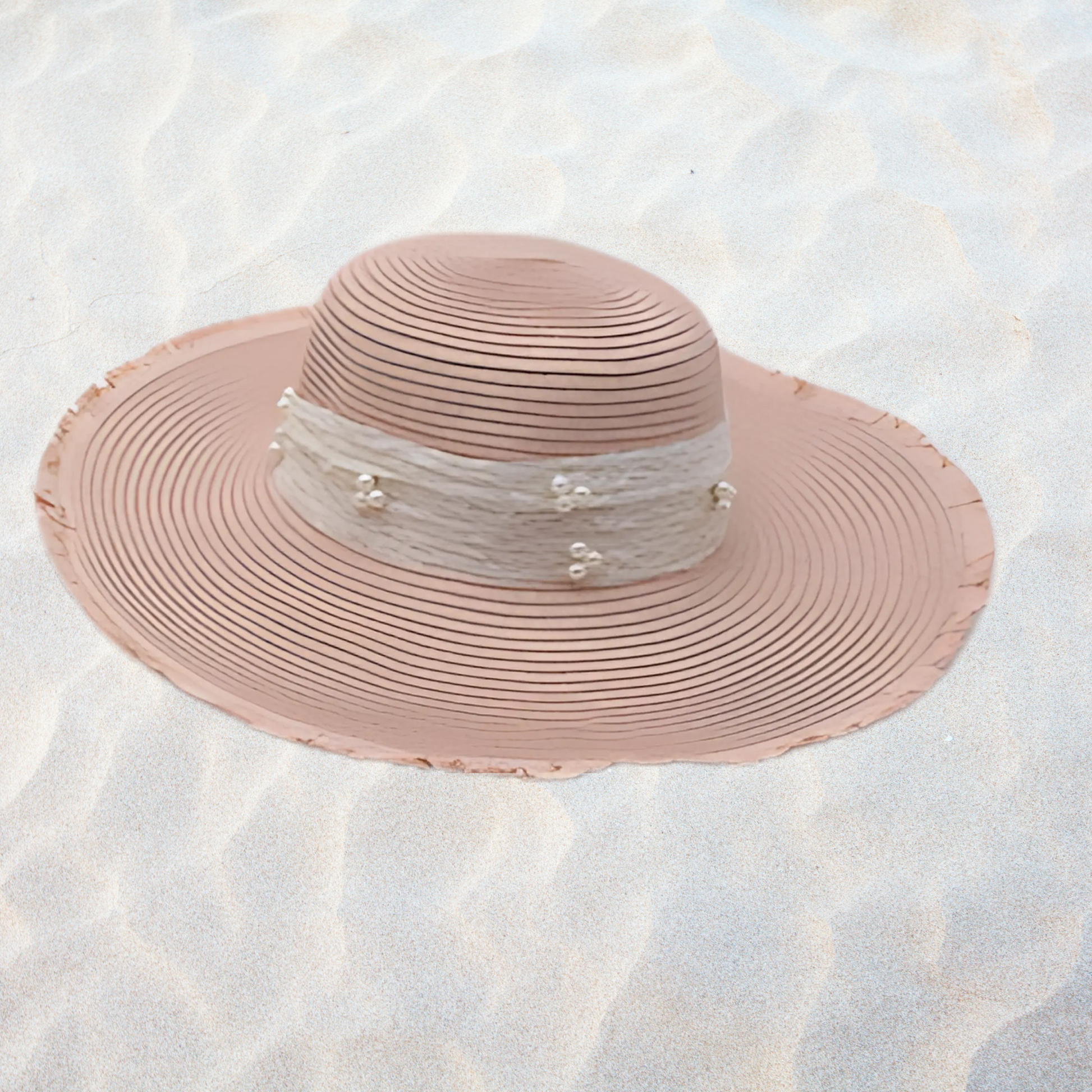 Pink straw hat with pearl embellishments on a textured white surface
