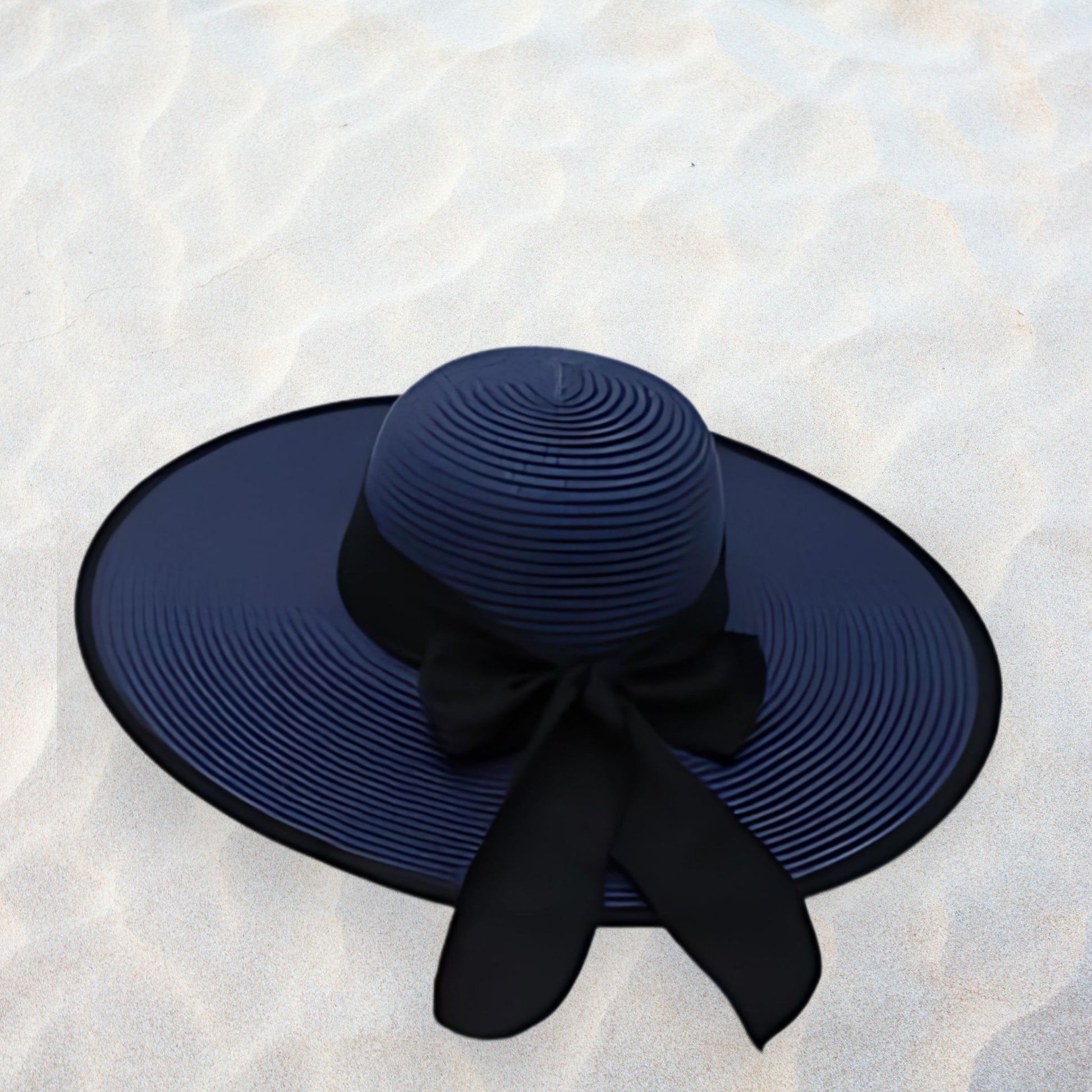 Navy blue sun hat with a wide brim and black ribbon on a sandy background