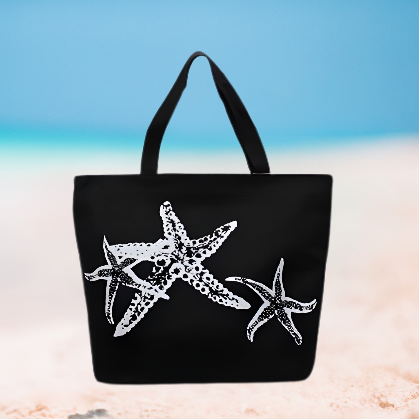 Black tote bag with white starfish design on a beach background