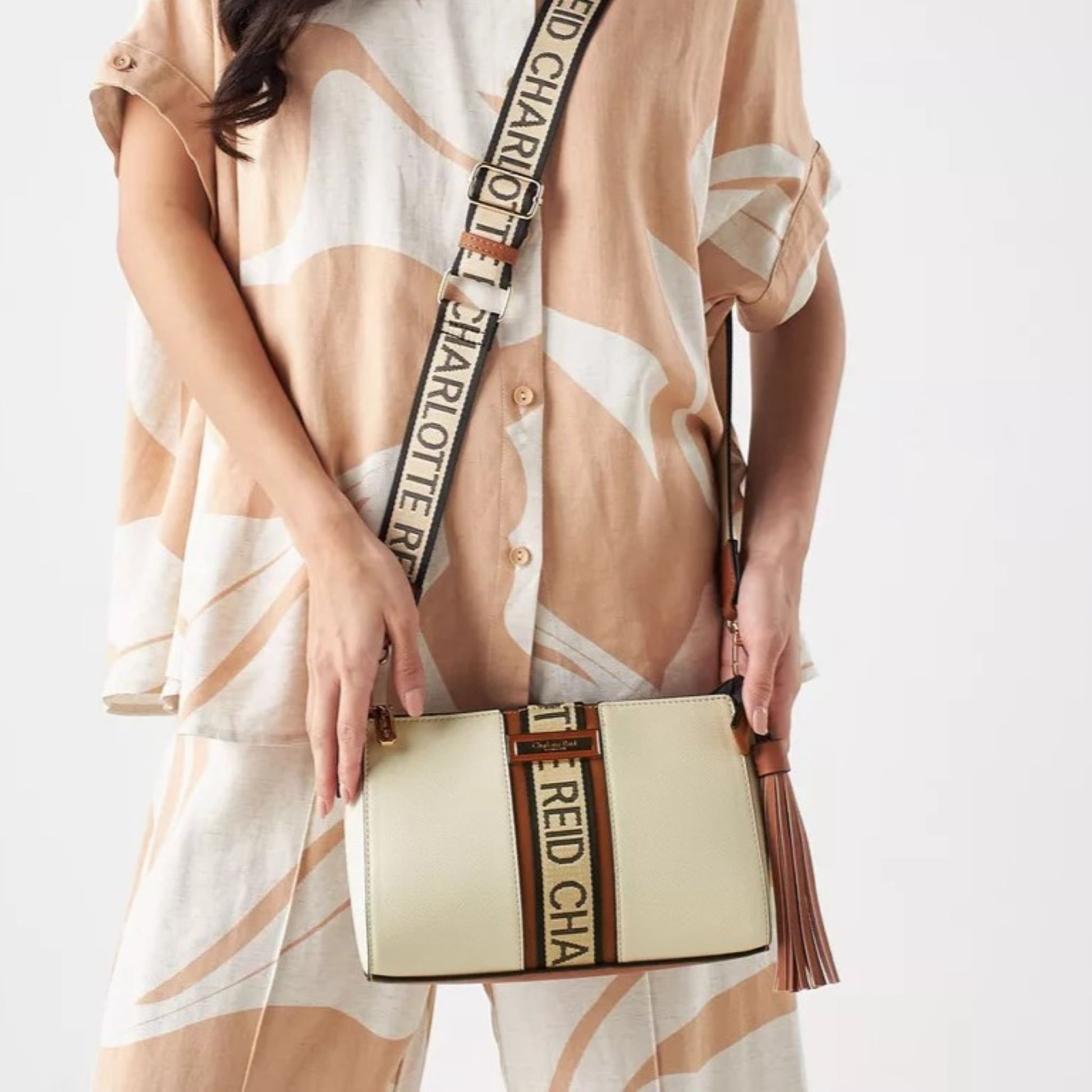 Beige pouch crossbody bag with removable and adjustable woven textured strap, with a monogram strip and removable tassel.