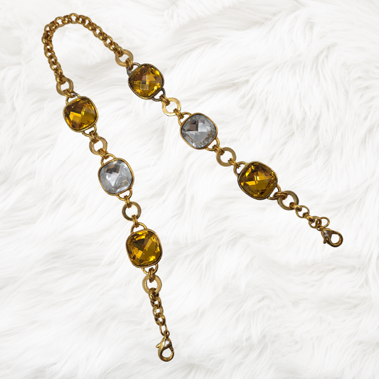 Gold chain bag chain with yellow and clear gemstones on a white textured background