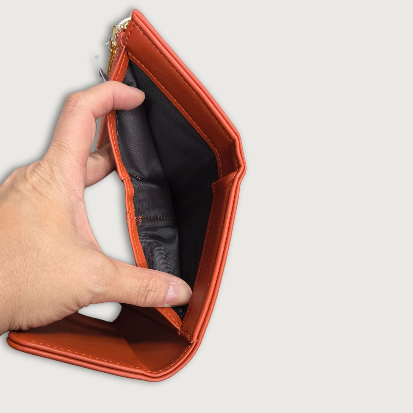 A red faux leather trifold wallet with a main compartment and multiple card slots, featuring a round emboss design on the clasp and gold hardware.