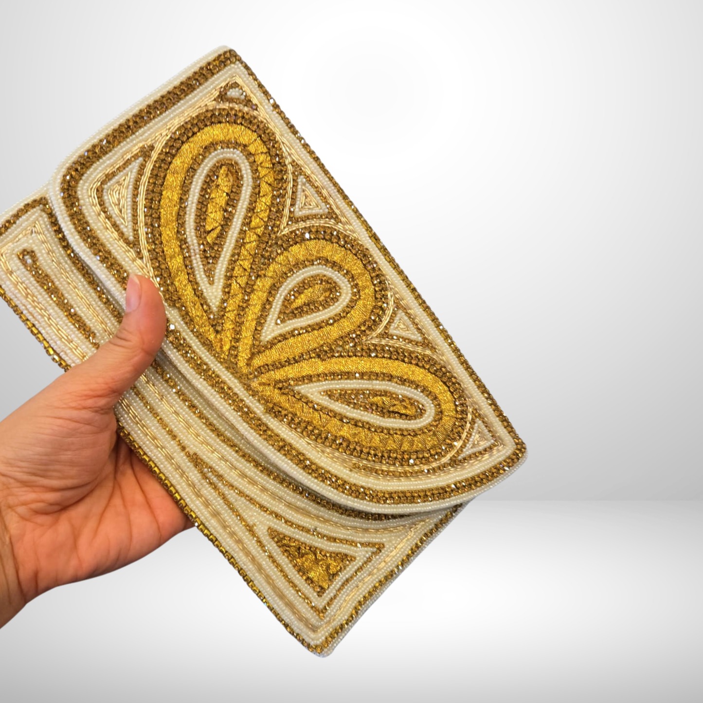 Hand holding a gold and beige embroidered clutch against a white background