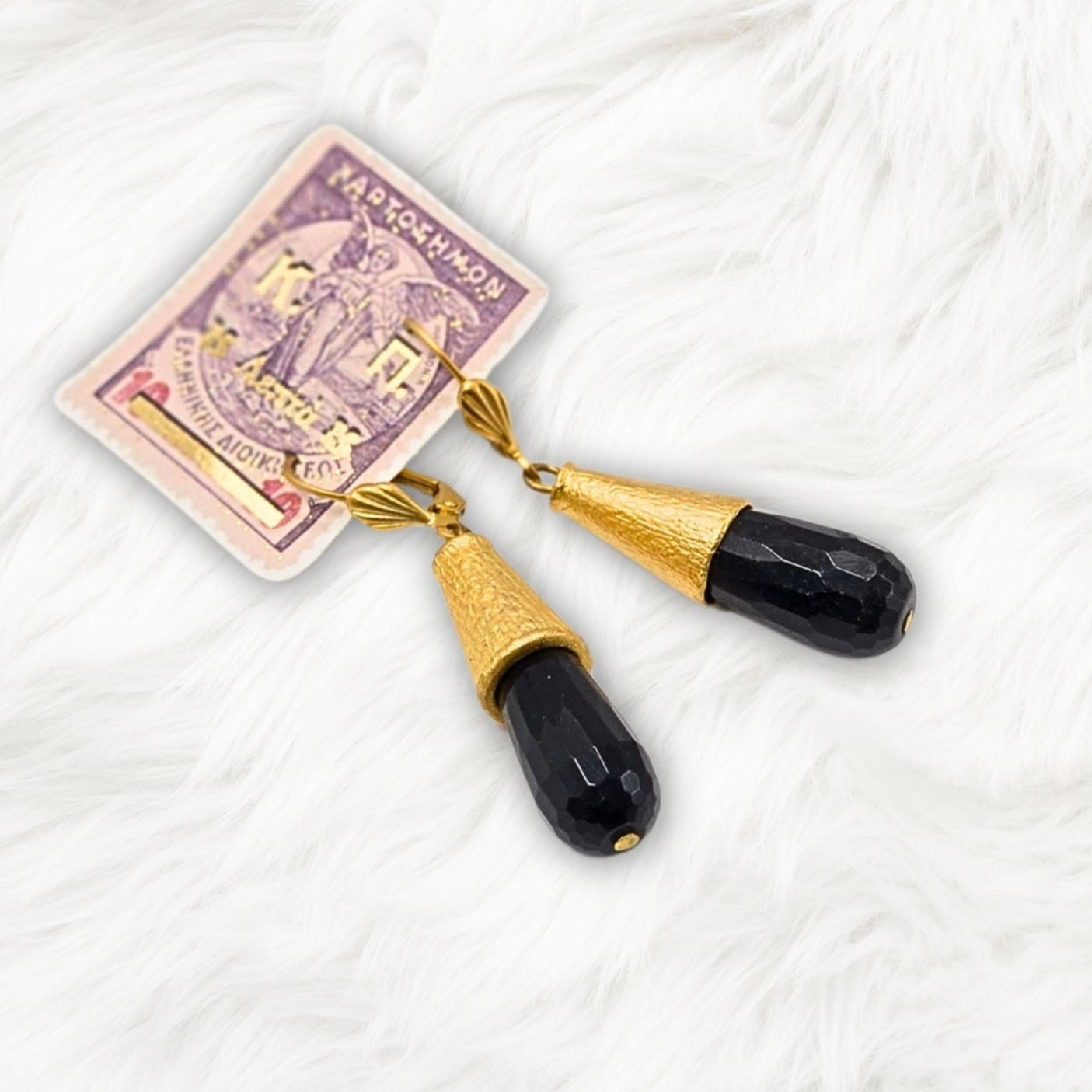 A pair of black onyx teardrop earrings with gold vermeil accents on a white furry surface.
