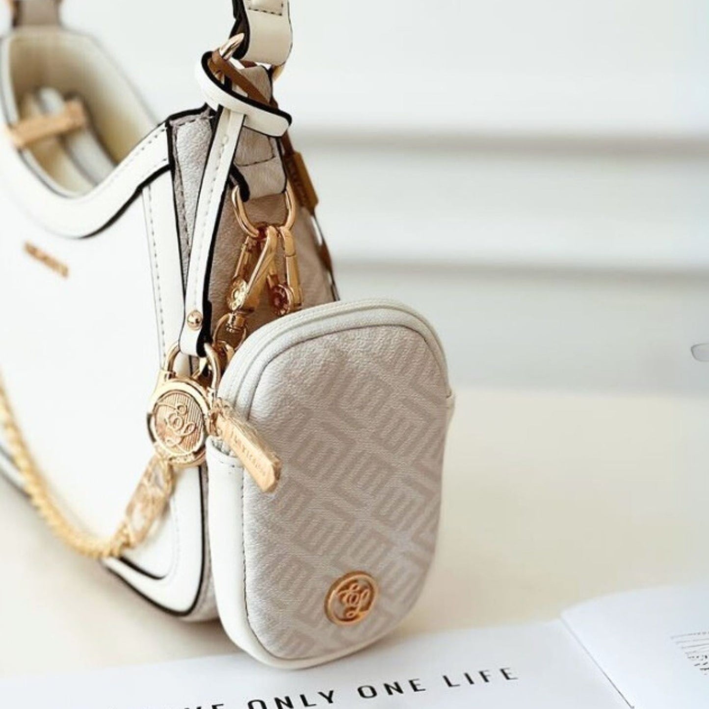 Small beige pouch with gold chain and keychain on a white surface
