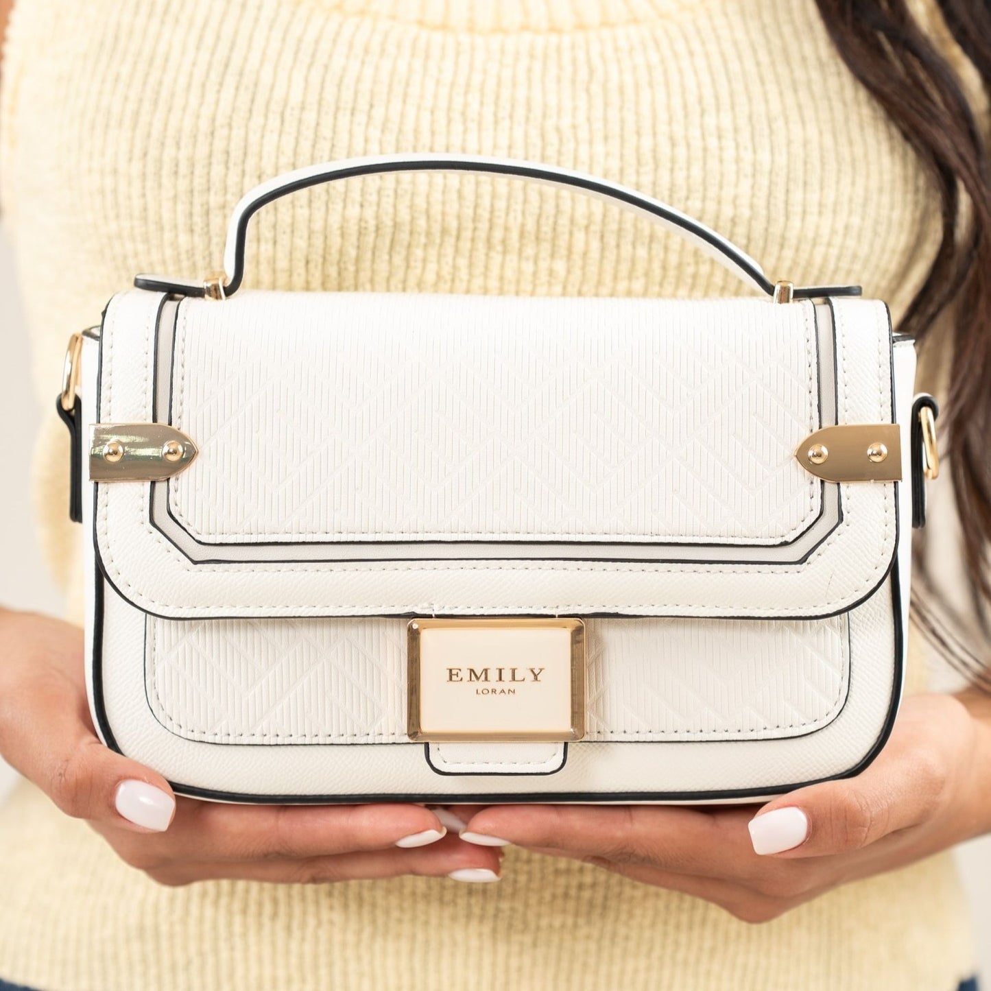 White handbag with gold accents held by a person wearing a beige sweater.
