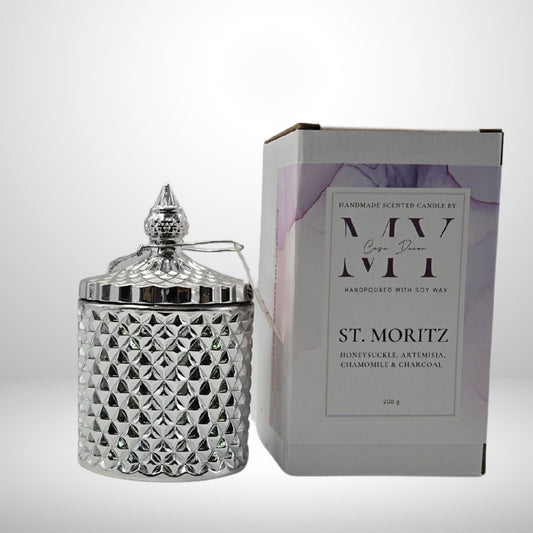 Silver textured candle jar with decorative lid next to its packaging on a white background