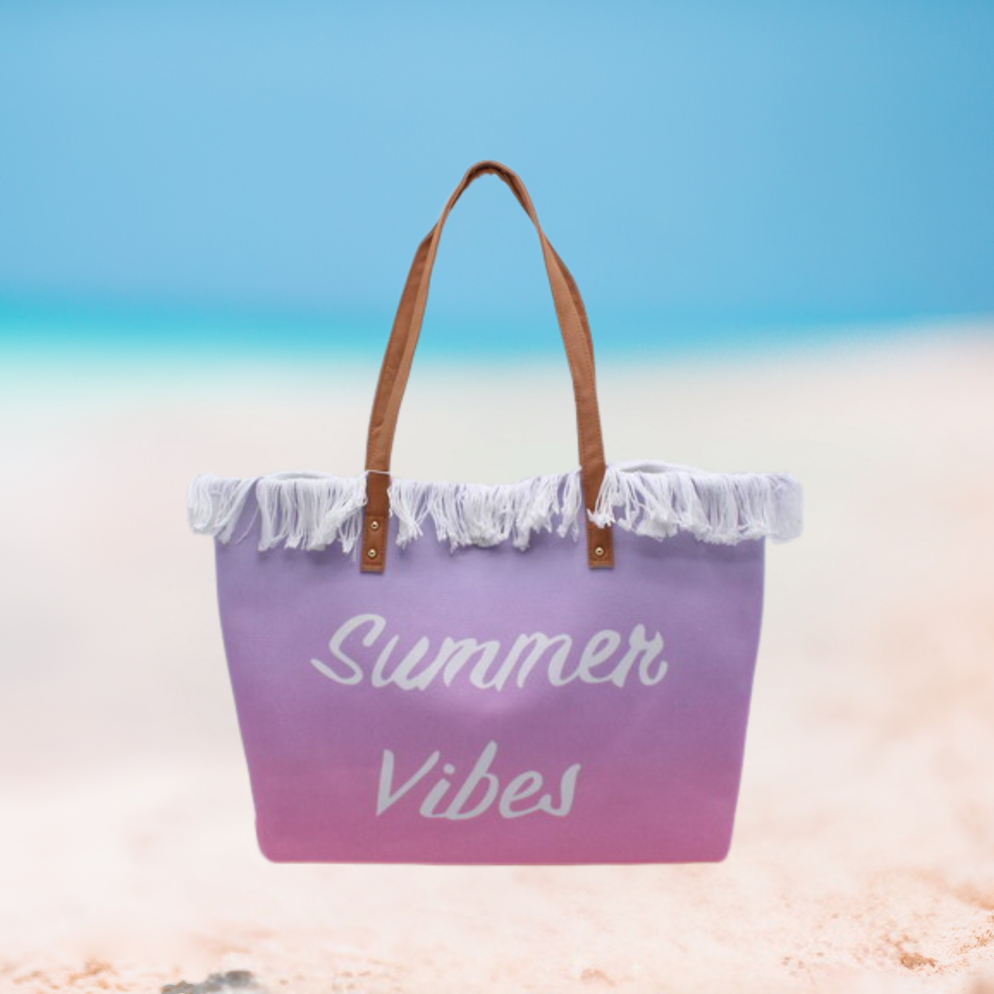 A purple-to-pink gradient beach tote bag with white fringe and brown handles, featuring the words 'Summer Vibes' in white script, set against a blurred beach and ocean background.