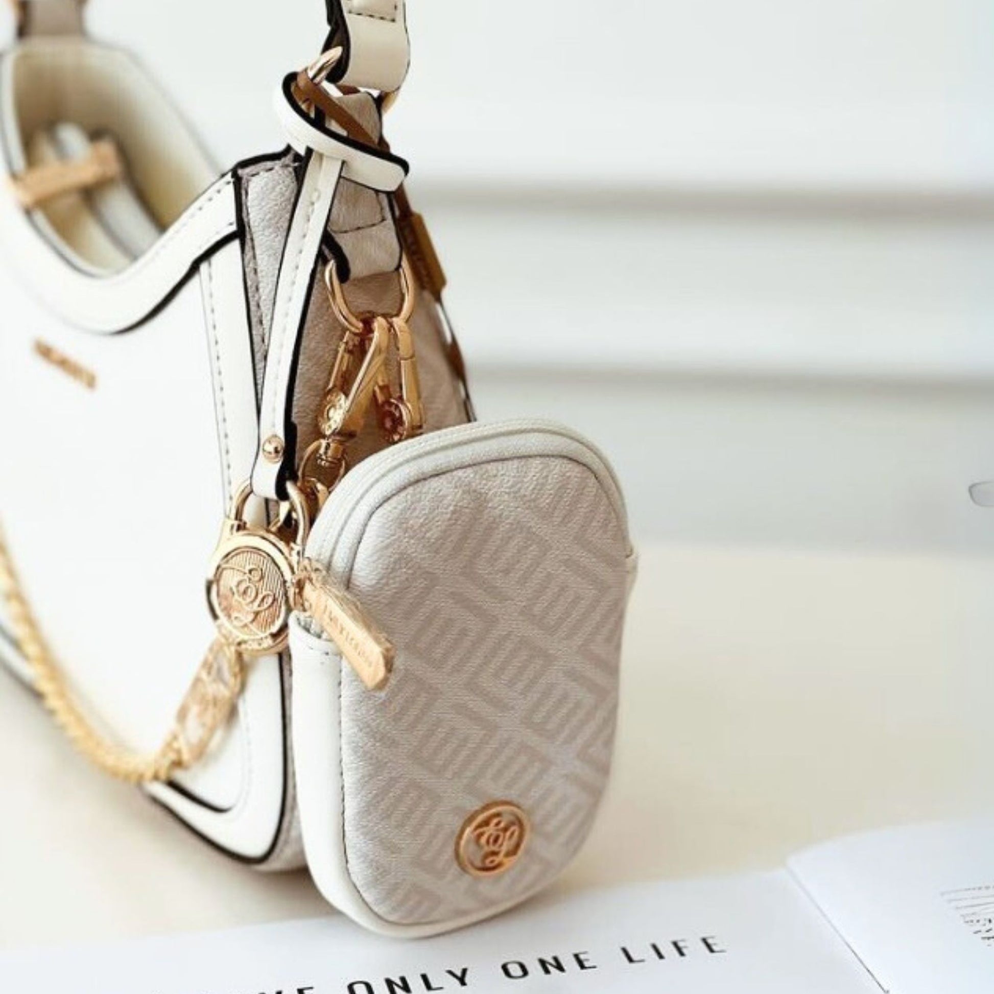 Small beige pouch with gold chain and keychain on a white surface