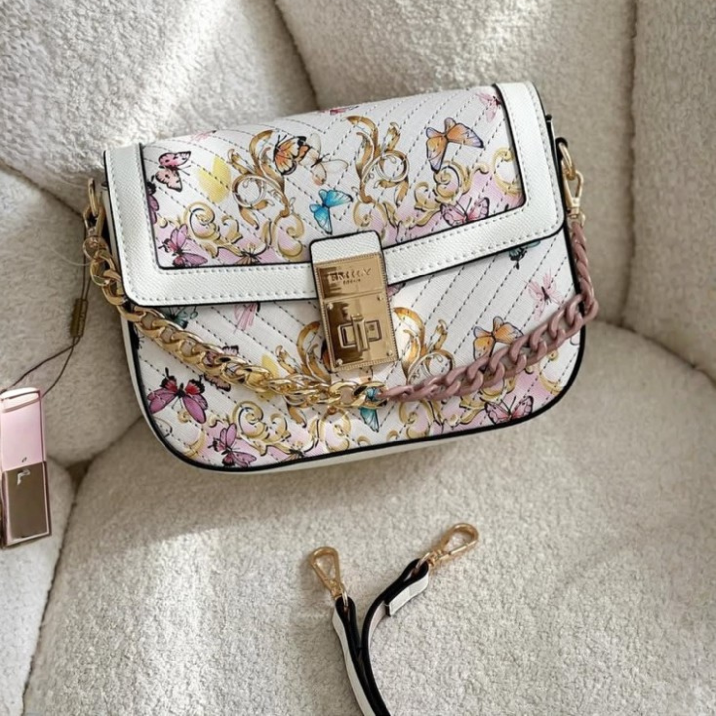White floral butterfly quilted crossbody bag with gold-tone chain accent, front lock closure, adjustable shoulder strap, and pastel printed design.