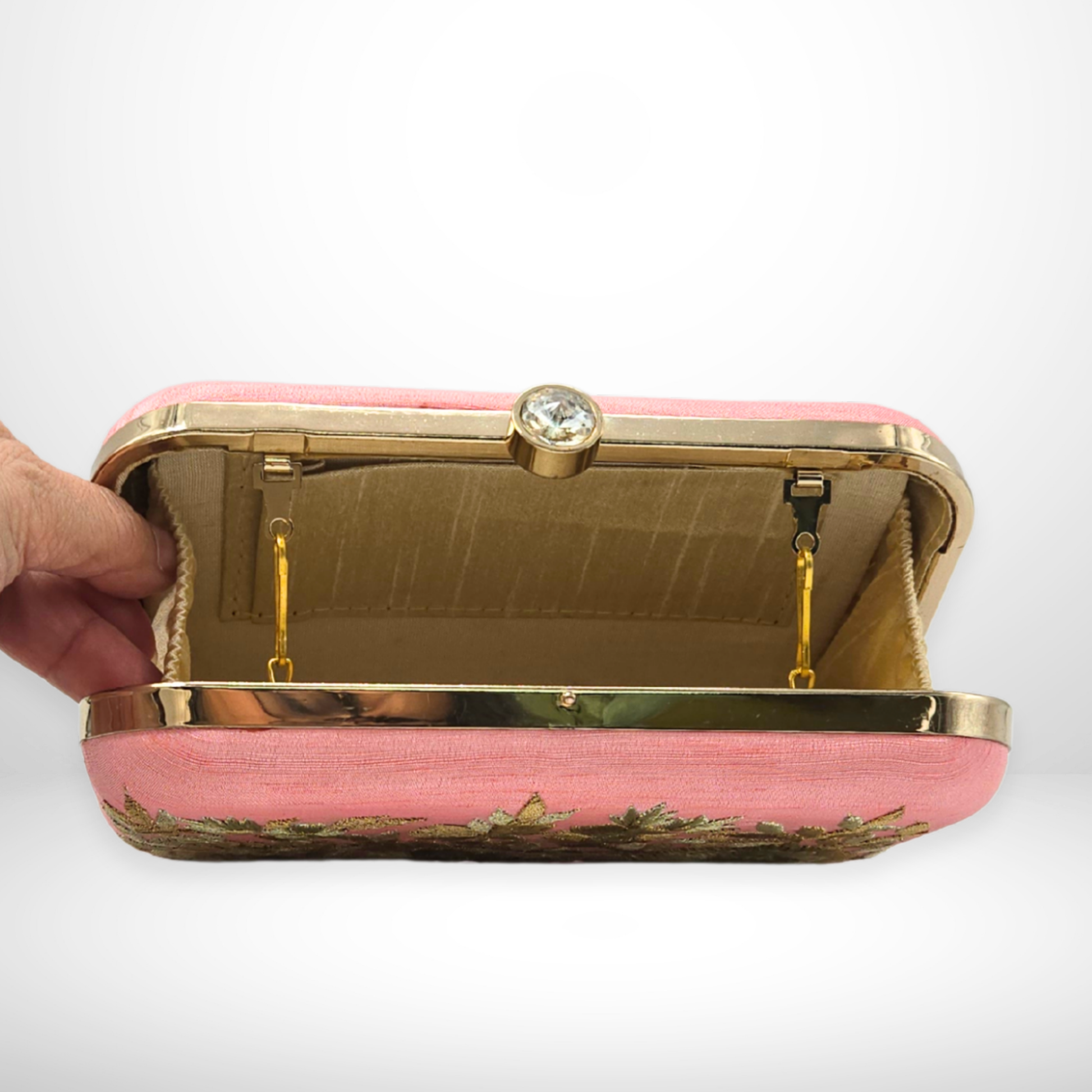 Pink clutch with gold frame held by a hand on a white background