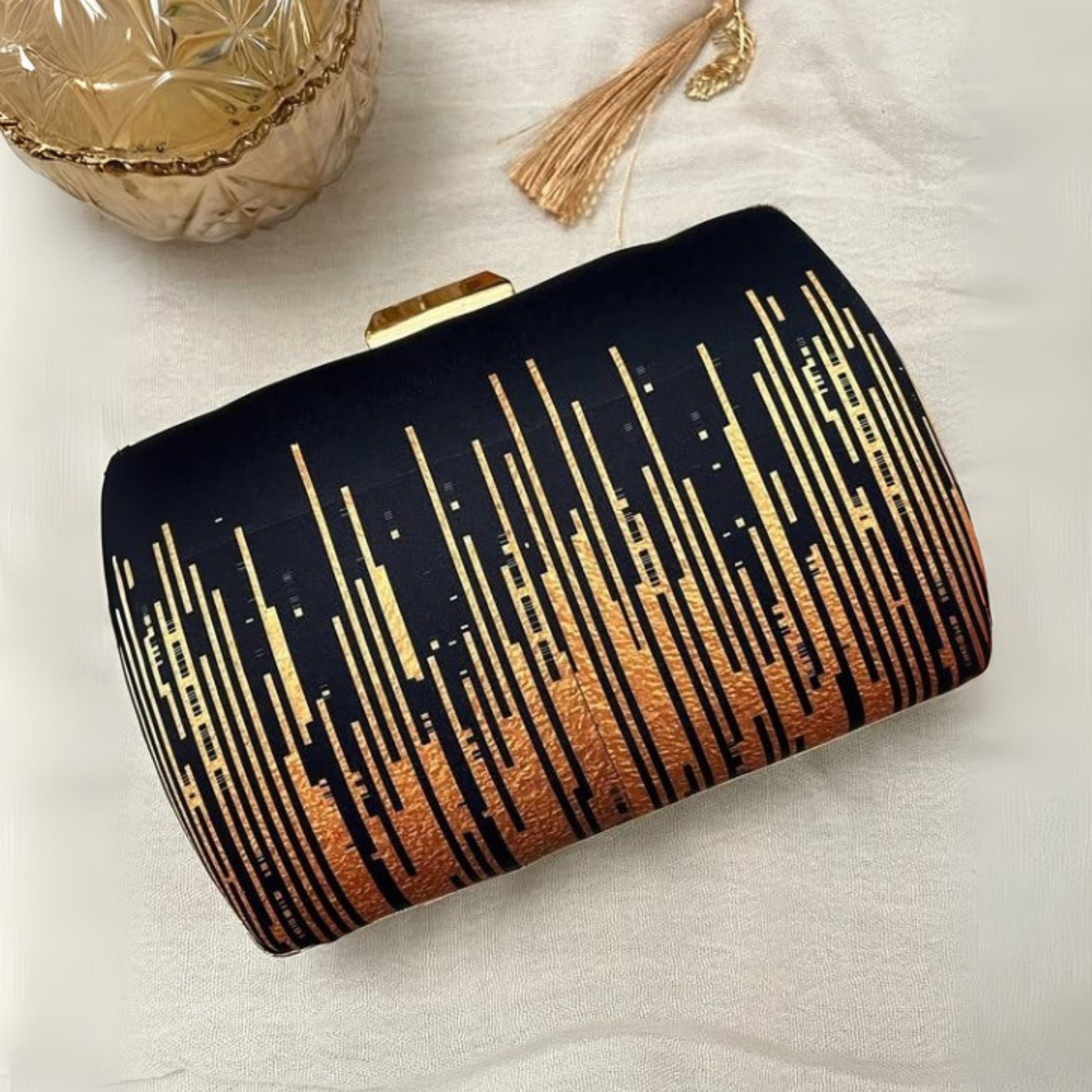 Black clutch with gold and bronze gradient pattern on a light background