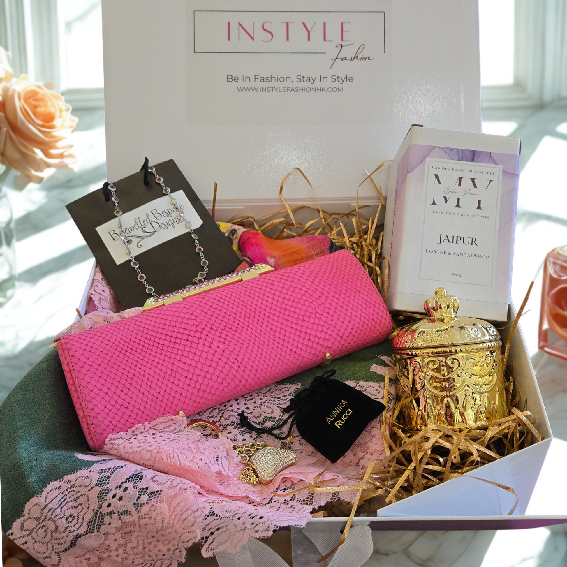 Gift box with pink fabric, jewelry, and decorative items on a marble surface.
