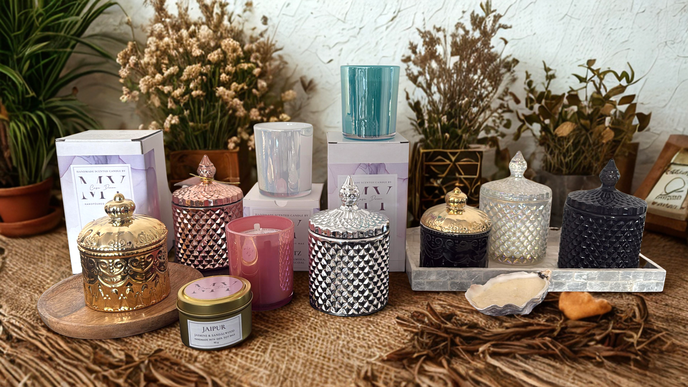 Assorted candles on a textured surface with plants and decorative items in the background